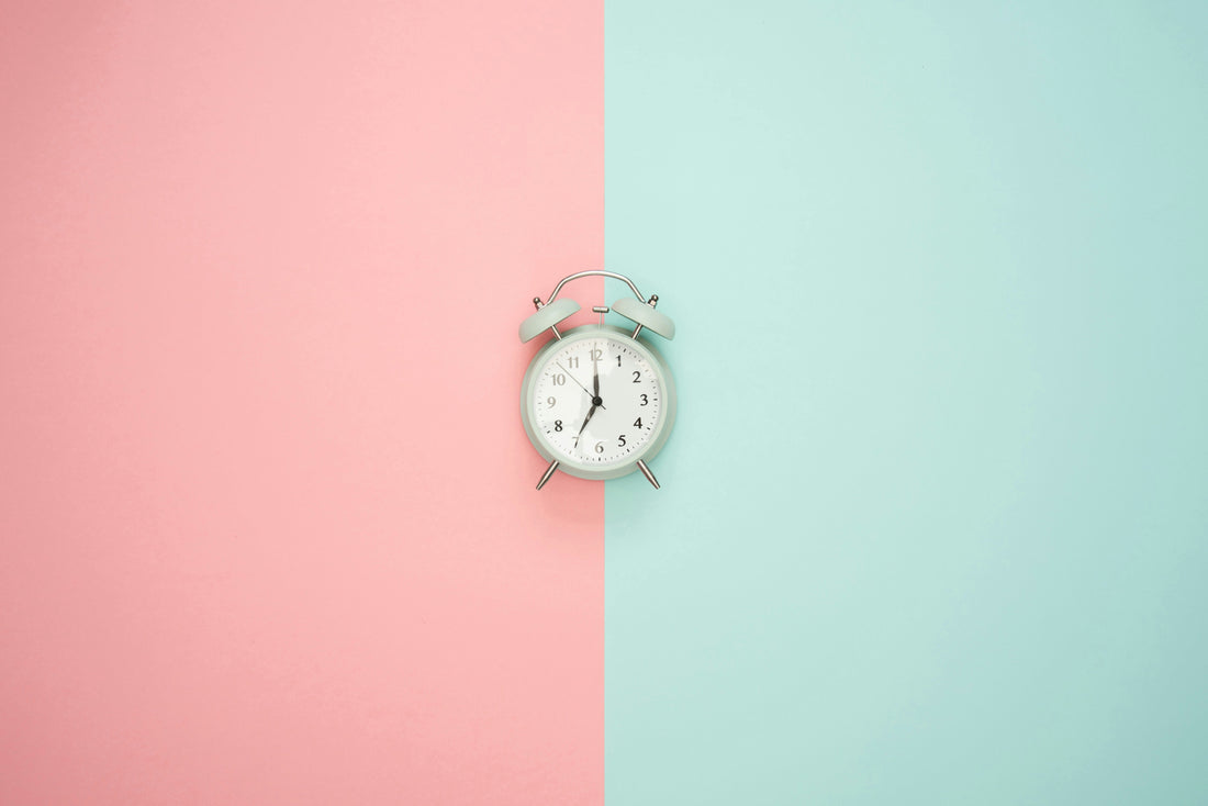 A vintage-style analog alarm clock centered on a pastel pink and mint green split background, symbolizing time management and focus.